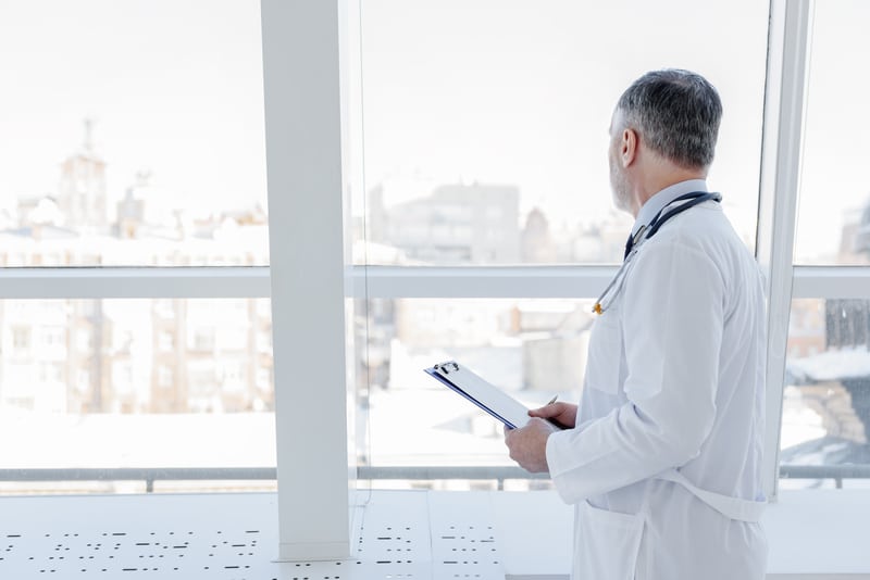 Doctor is looking out the window, thinking about his patient.