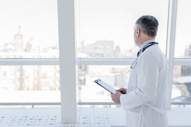 Doctor is looking out the window, thinking about his patient.